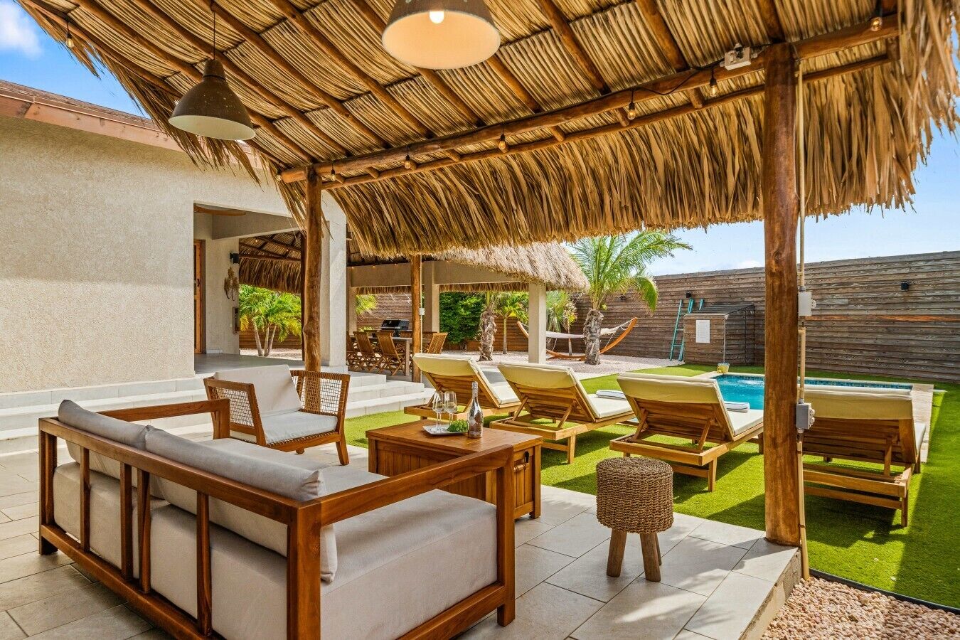Eine Terrassengaststätte mit Holzmöbeln, einem Reetdach und einem Pool.
