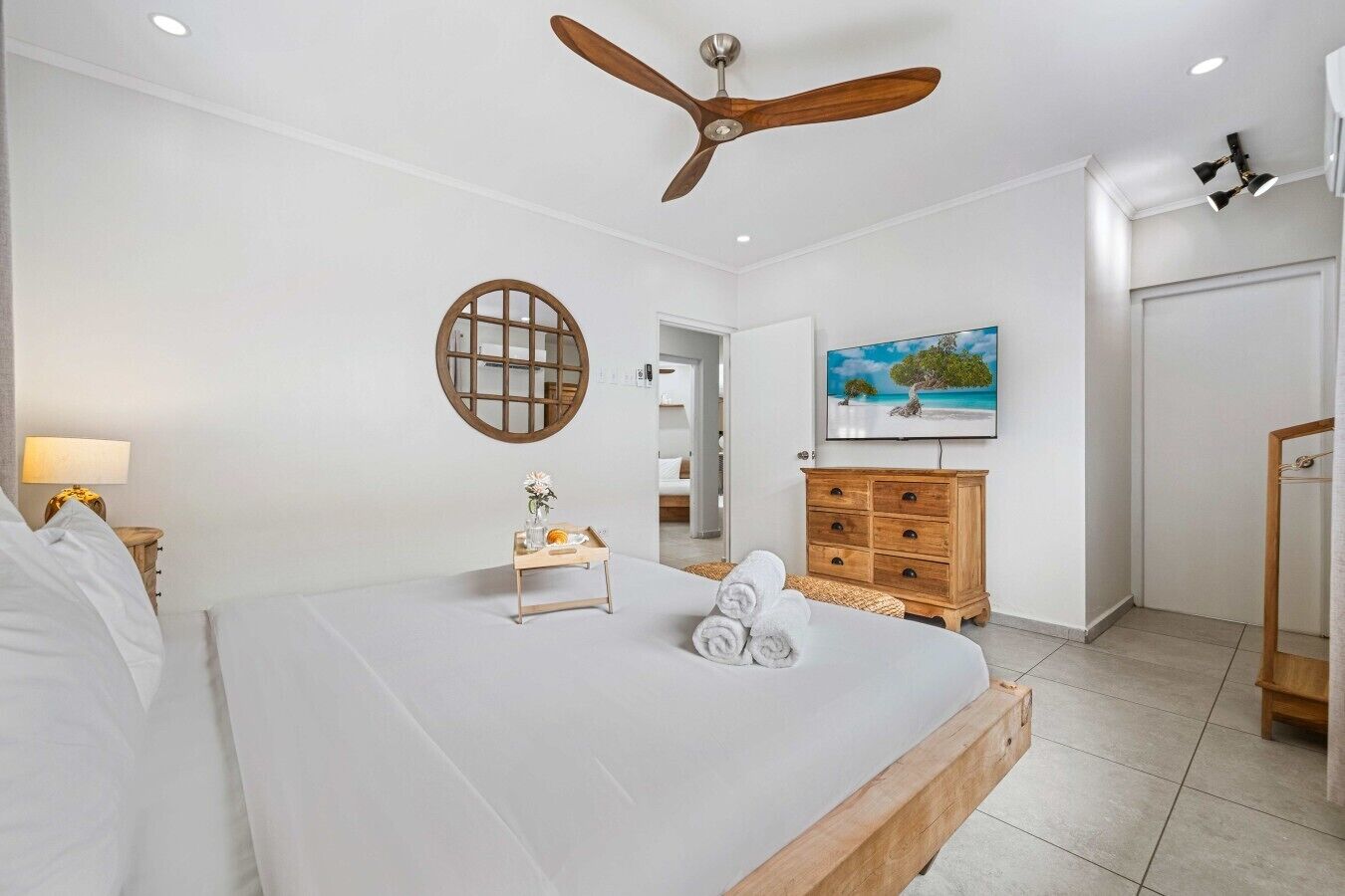 A hotel room with a bed, a ceiling fan, a wooden dresser, a painting, and a small table with towels.