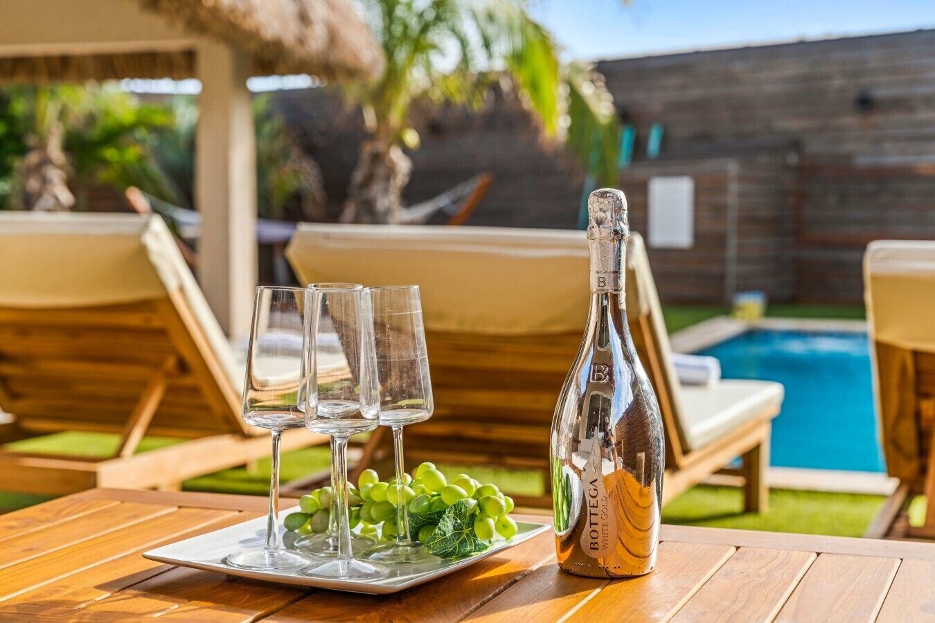 A table with a bottle of white wine, three glasses, and a plate of grapes.