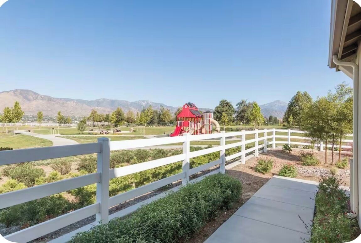 A fenced outdoor area with a playground, a red building, and a mountain range in the background.