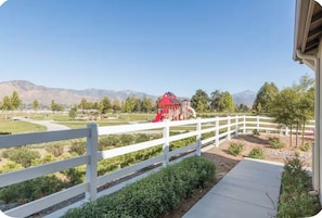 A fenced outdoor area with a playground, a red building, and a mountain range in the background. - Redlands Cozy One Bedroom Suite w/Access to a park (Redlands)