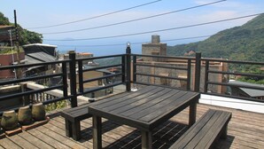 Um deck de madeira com mesa e bancos, com vista para uma paisagem montanhosa e edifícios ao longe.
