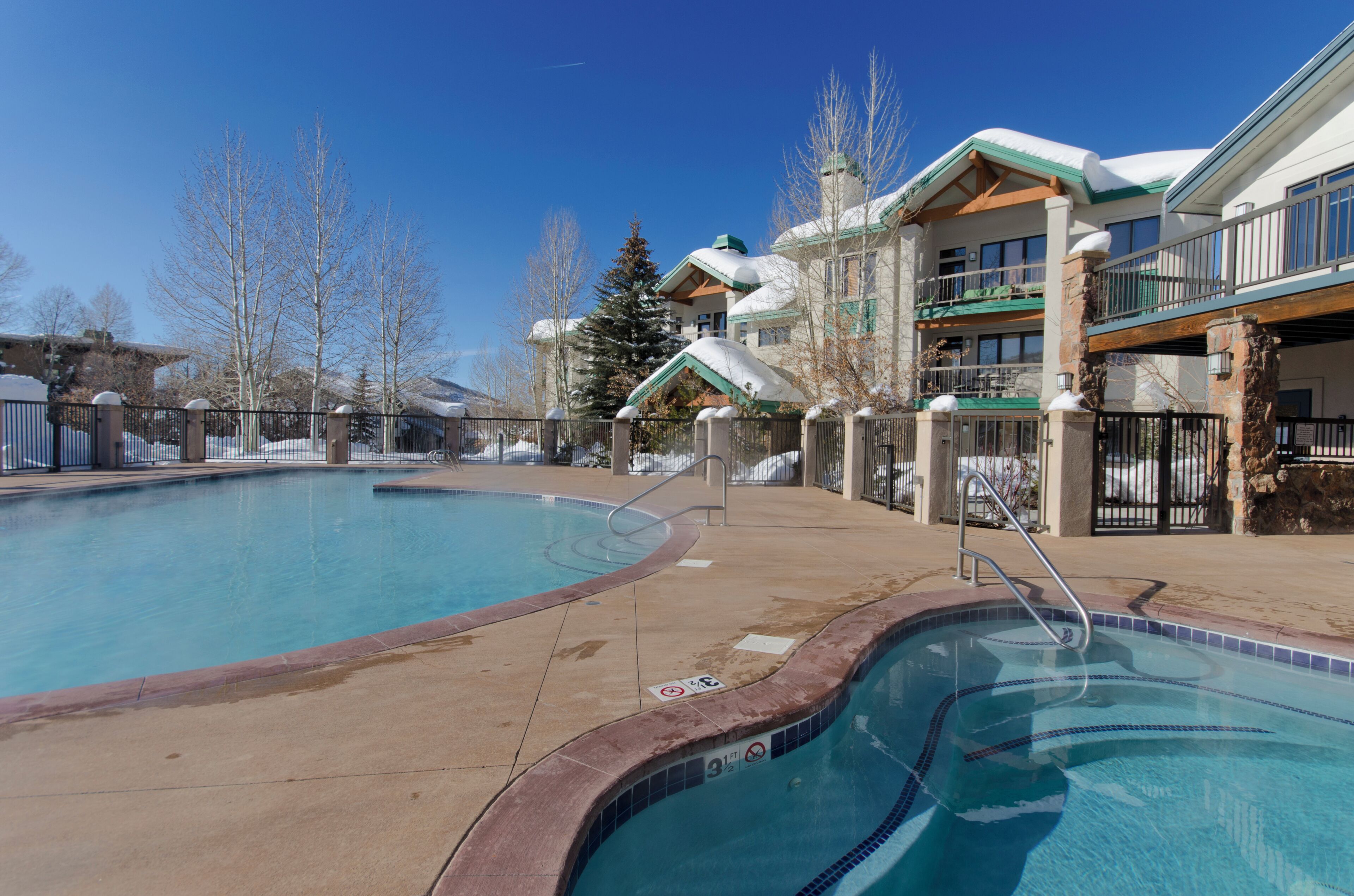 A pool area with a clear blue pool, a stone border, and a wooden deck.