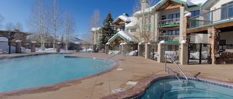 A pool area with a clear blue pool, a stone border, and a wooden deck.