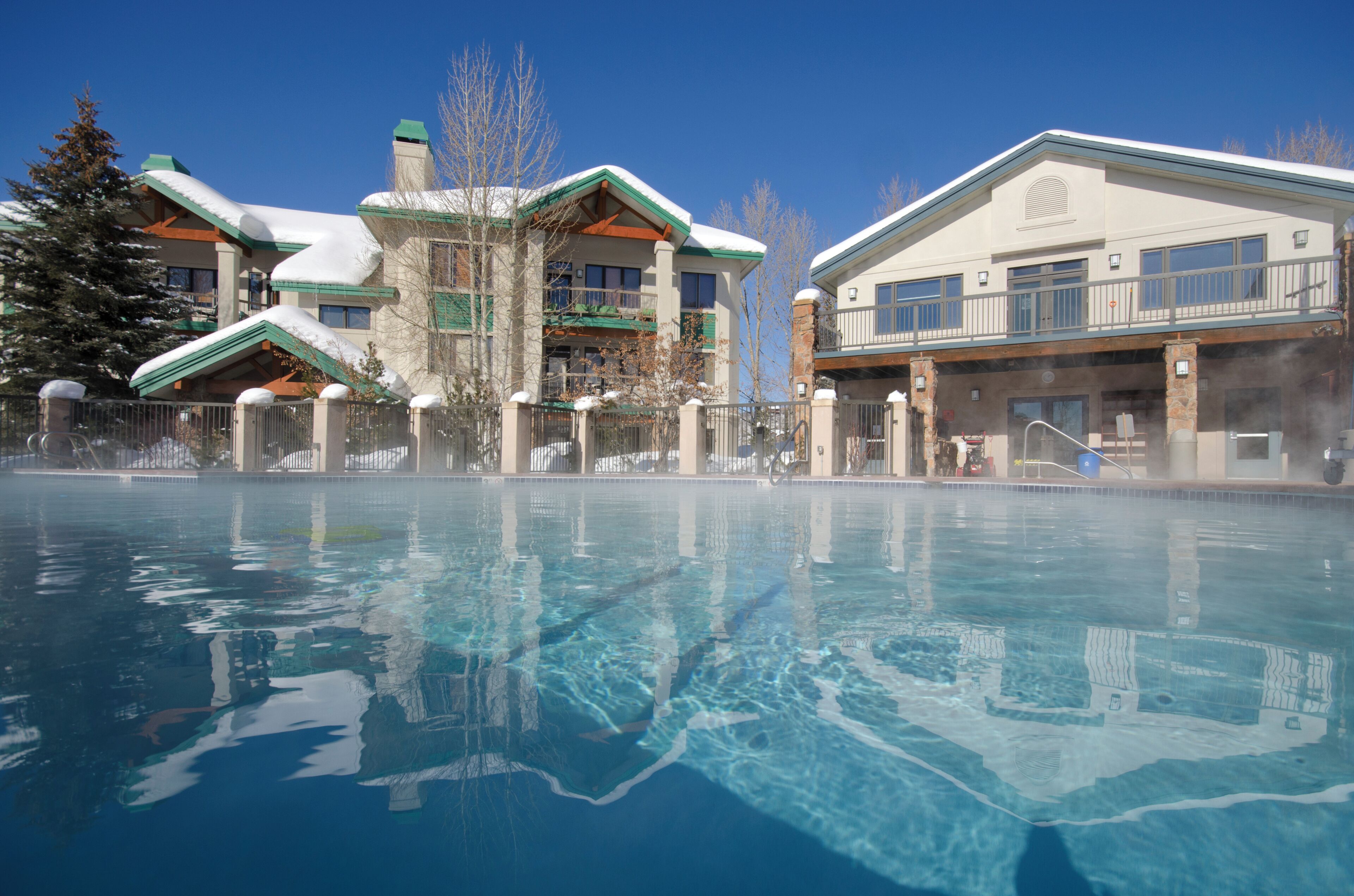A hotel with a swimming pool, a covered area, and a building with a green roof.