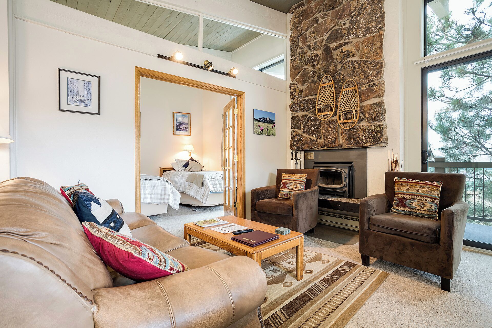 A cozy living room with a stone fireplace, a sofa, a chair, and a bed with a view of the outdoors.