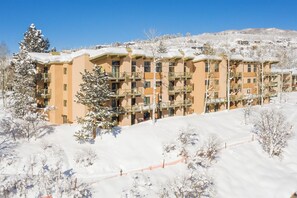 Ein mehrstöckiges Hotel mit Balkonen, umgeben von schneebedeckten Bäumen und einer Skipiste.