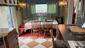 Une pièce chaleureuse avec un sol à carreaux, une table à manger avec des chaises, un petit coin cuisine et une fenêtre avec des rideaux.