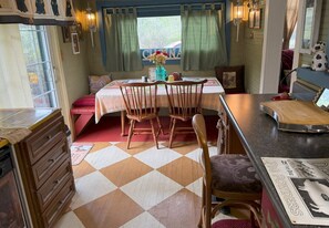 A cozy room with a checkered floor, a dining table with chairs, a small kitchen area, and a window with curtains. - Peaceful and cozy 1-bedroom historic creek-side cabin in Glenville with AC (Glenville)