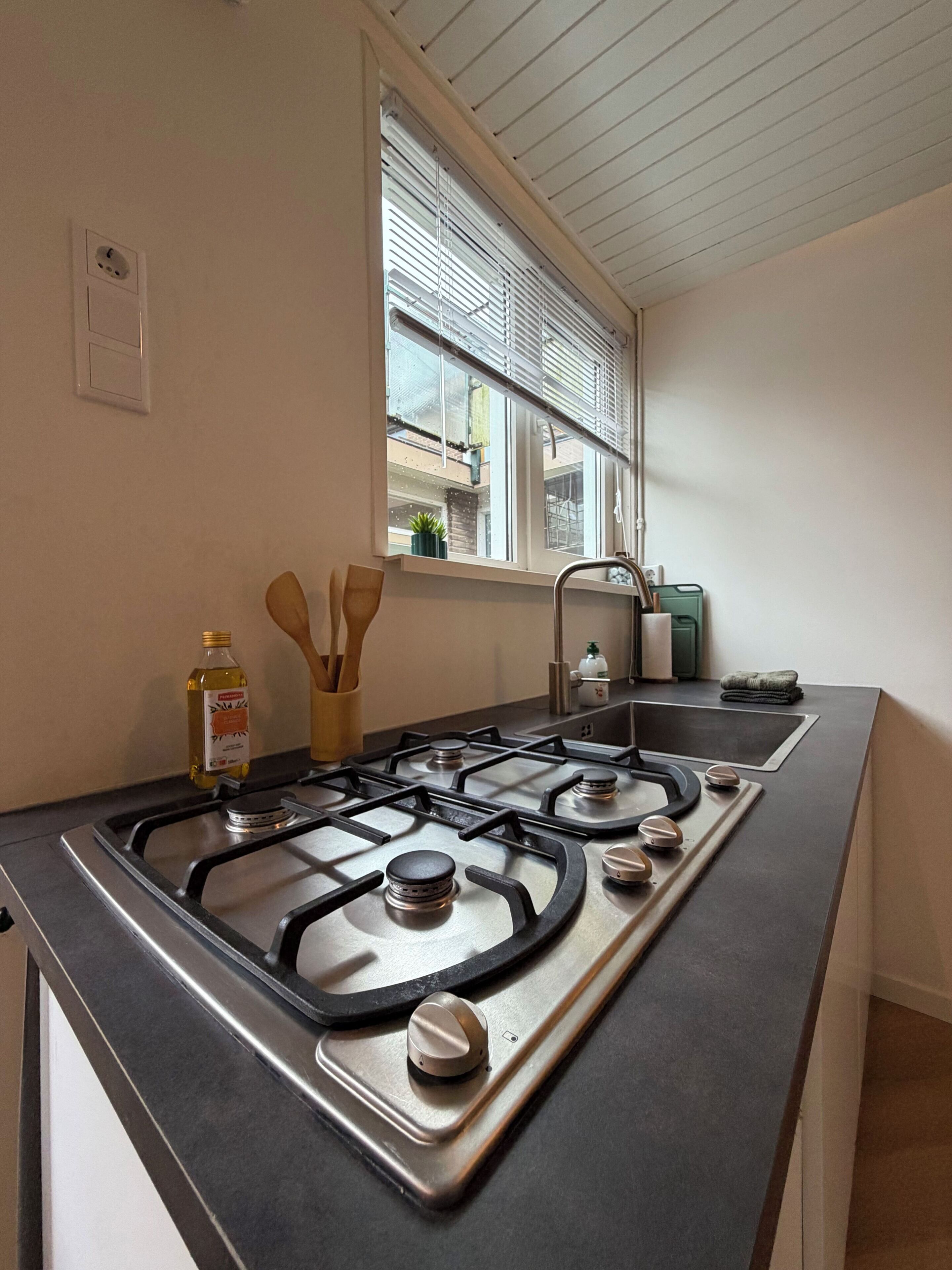 Una cocina con estufa a gas, una ventana con persianas y un lavamanos.