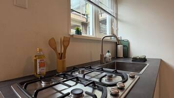 Una cocina con estufa a gas, una ventana con persianas y un lavamanos.