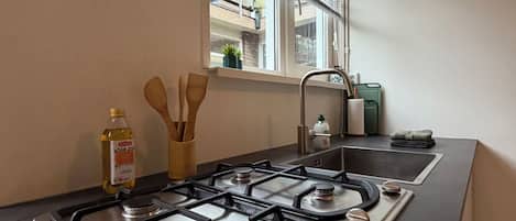 Une cuisine équipée d’une cuisinière à gaz, d’une fenêtre avec des stores et d’un évier.