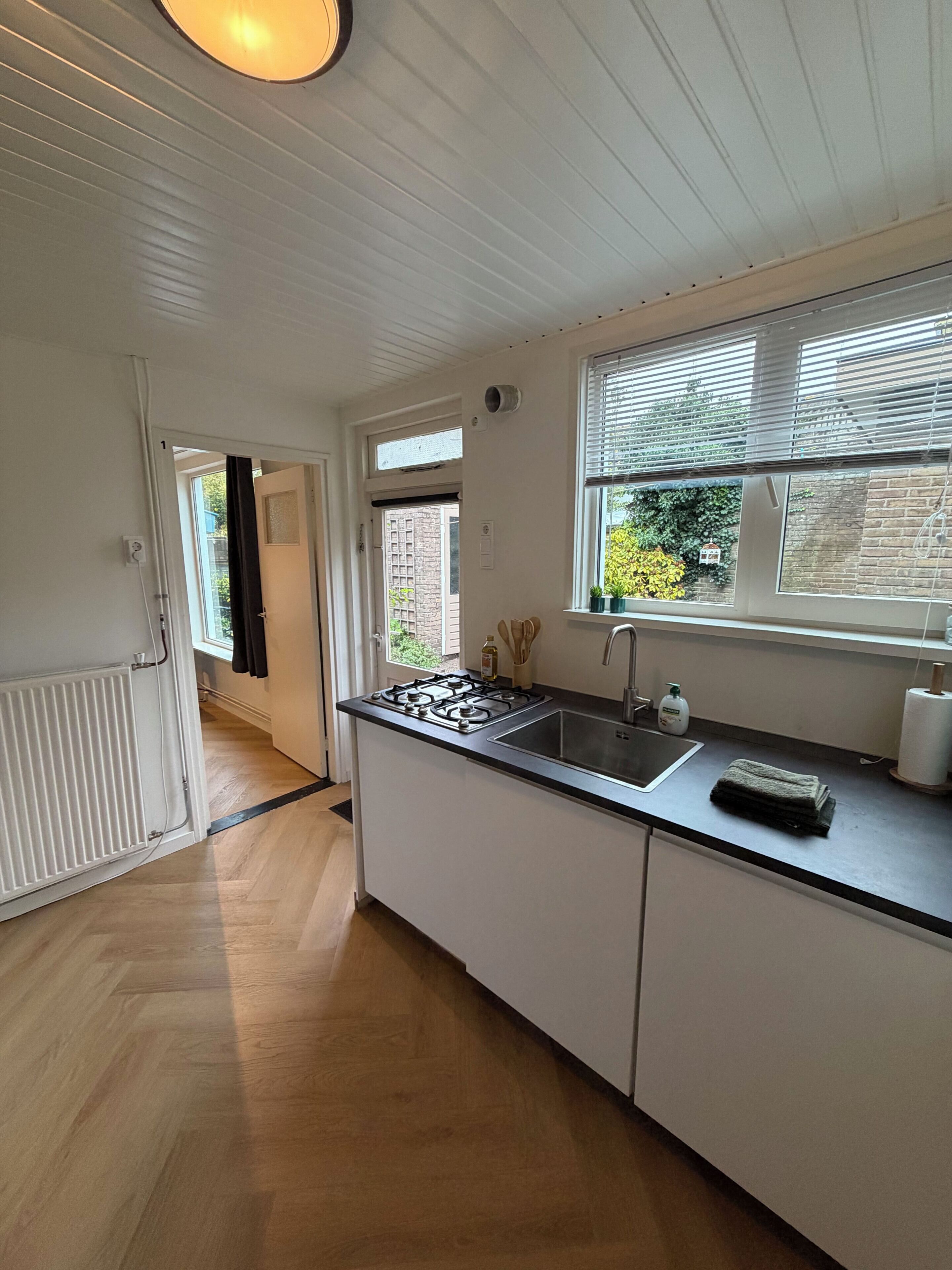 A modern kitchen with a gas stove, sink, and window with blinds.