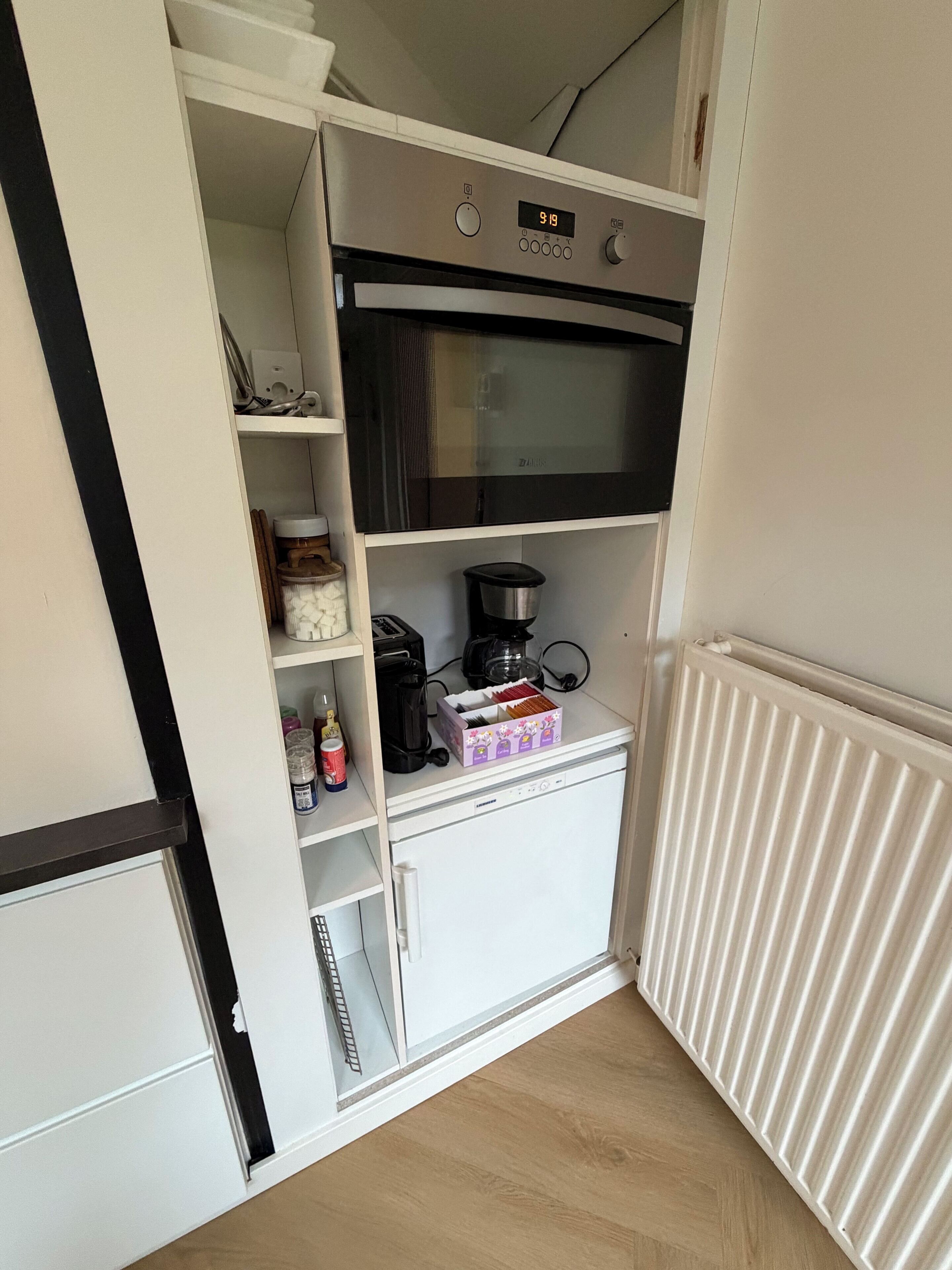 Una kitchenette compacta con microondas, cafetera y estanterías para guardar.