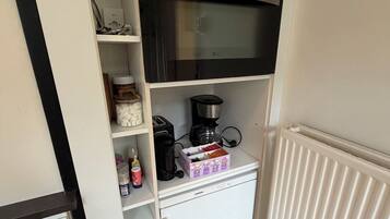 Una kitchenette compacta con microondas, cafetera y estanterías para guardar.