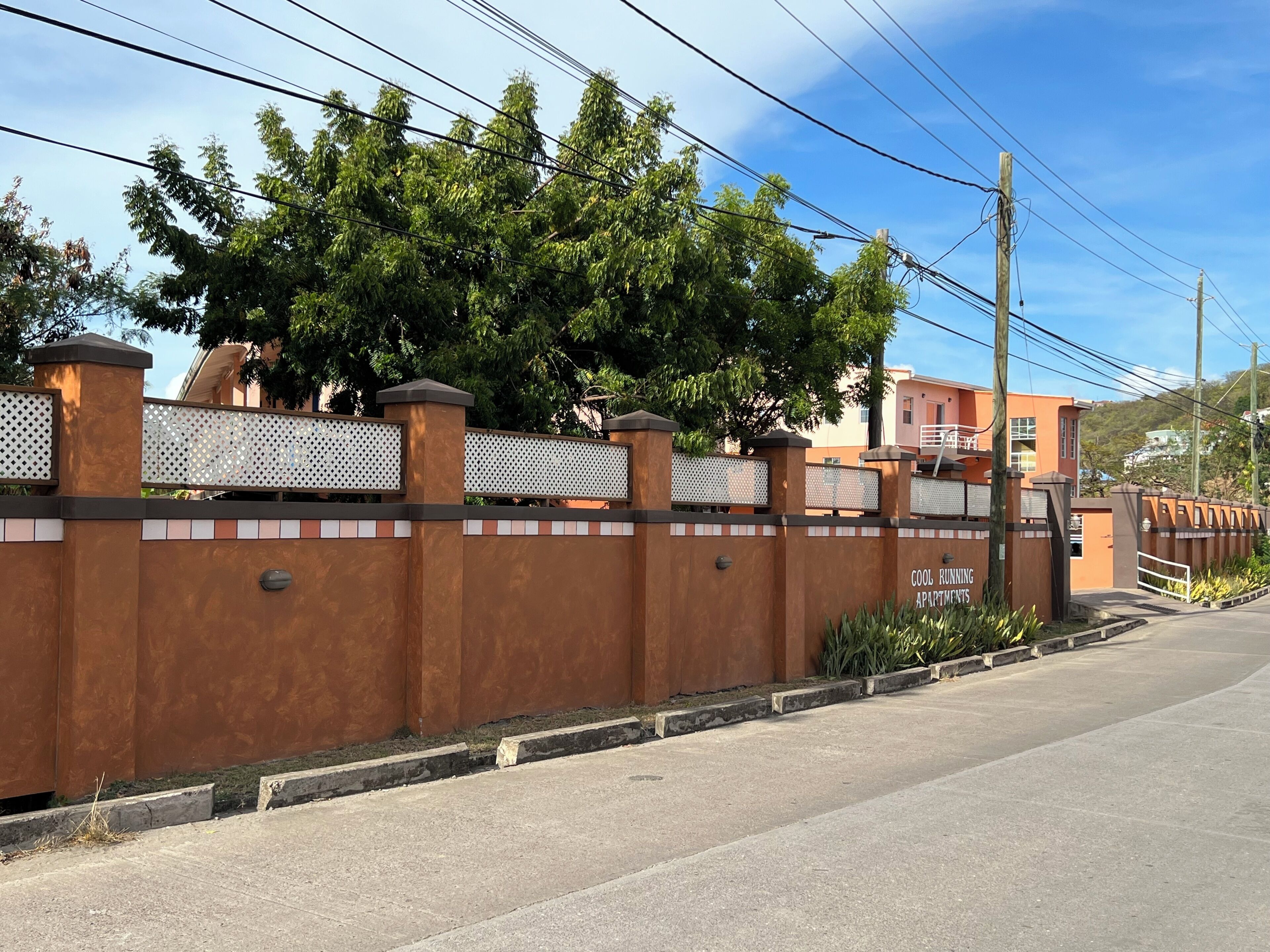A gated residential area with a paved road, a fence with a decorative pattern, and a building with a sign indicating 'Cool Running Apartments'.