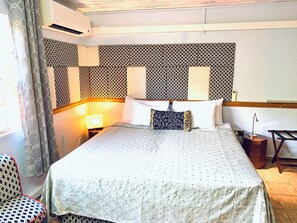 A hotel room with a bed, bedside lamps, patterned wallpaper, and a window with curtains. - A/C True Blue Apt base -perfect for SGU Airport - Yacht life, Beach, Fast WiFi (Saint George's)