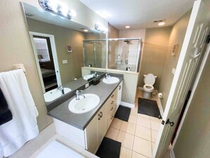 Un baño con dos lavamanos, un espejo grande, cabina de ducha y un inodoro.