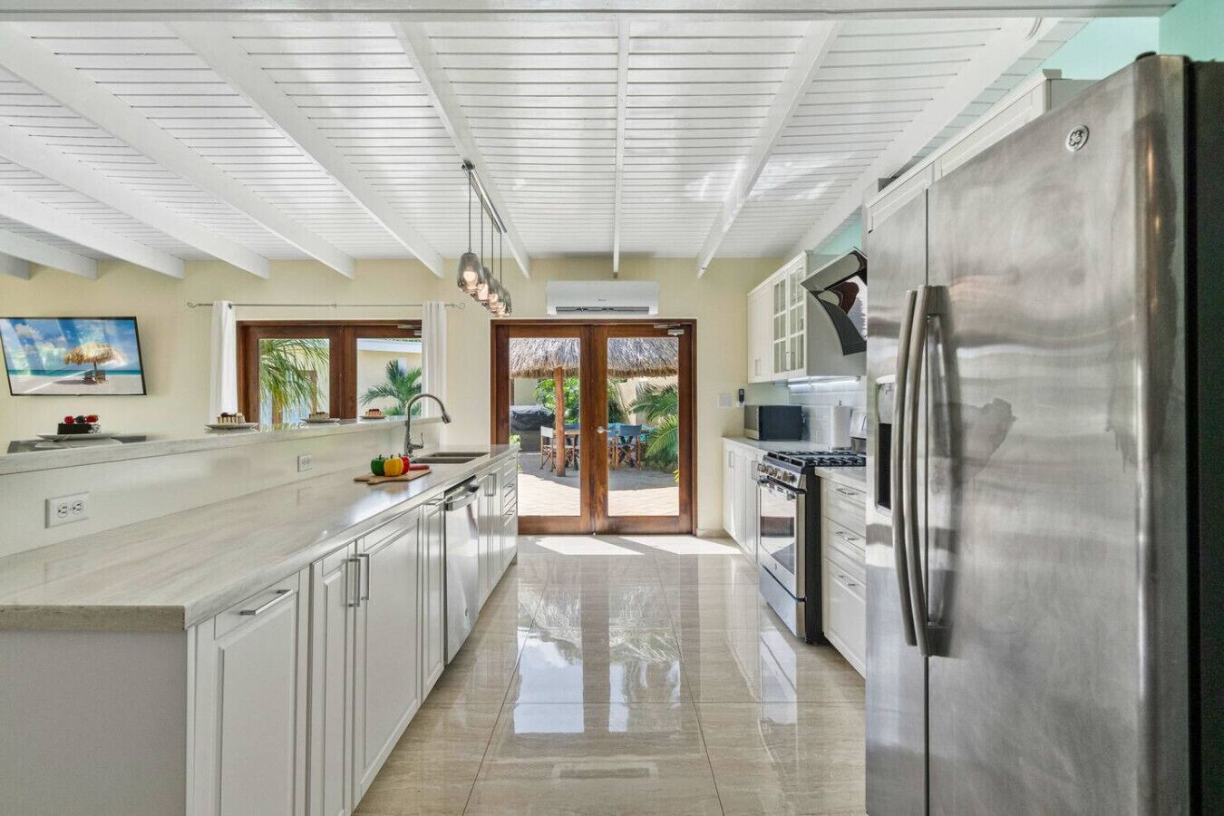 A kitchen with a stainless steel refrigerator, a stove, and a microwave. There is a large window and a door leading to an outdoor area.
