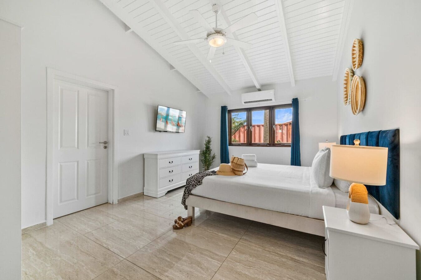 Une chambre à coucher comprenant un lit, une table de chevet, une lampe, un téléviseur, une fenêtre avec des rideaux et un ventilateur de plafond.