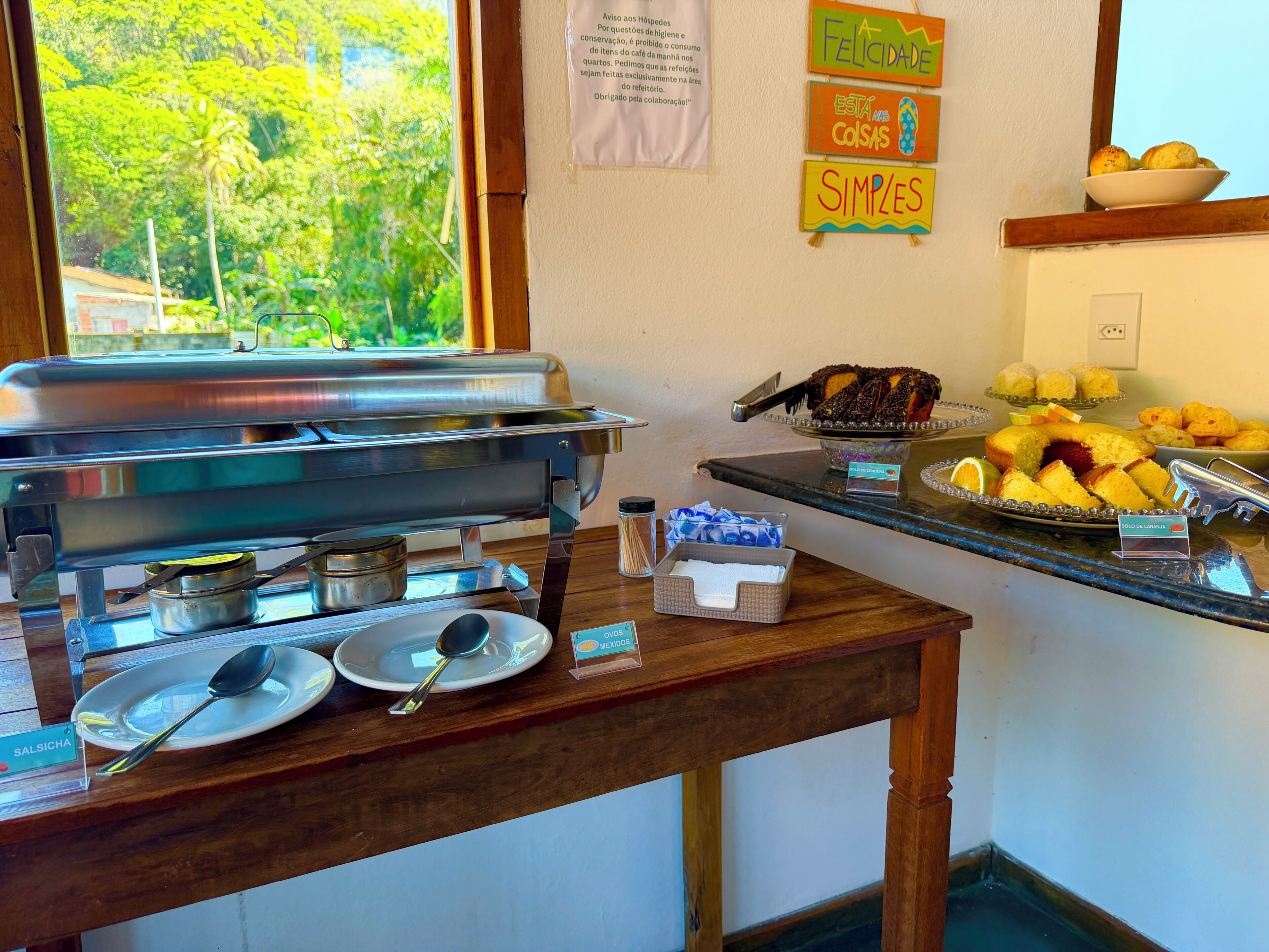 Un buffet composé d’un présentoir en acier inoxydable, d’un saladier rempli de fruits et d’une pancarte indiquant « Salsicha » (saucisse).