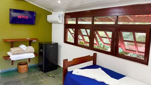 A room with a bed, a television, a refrigerator, a window with a view, and a wall-mounted air conditioner.