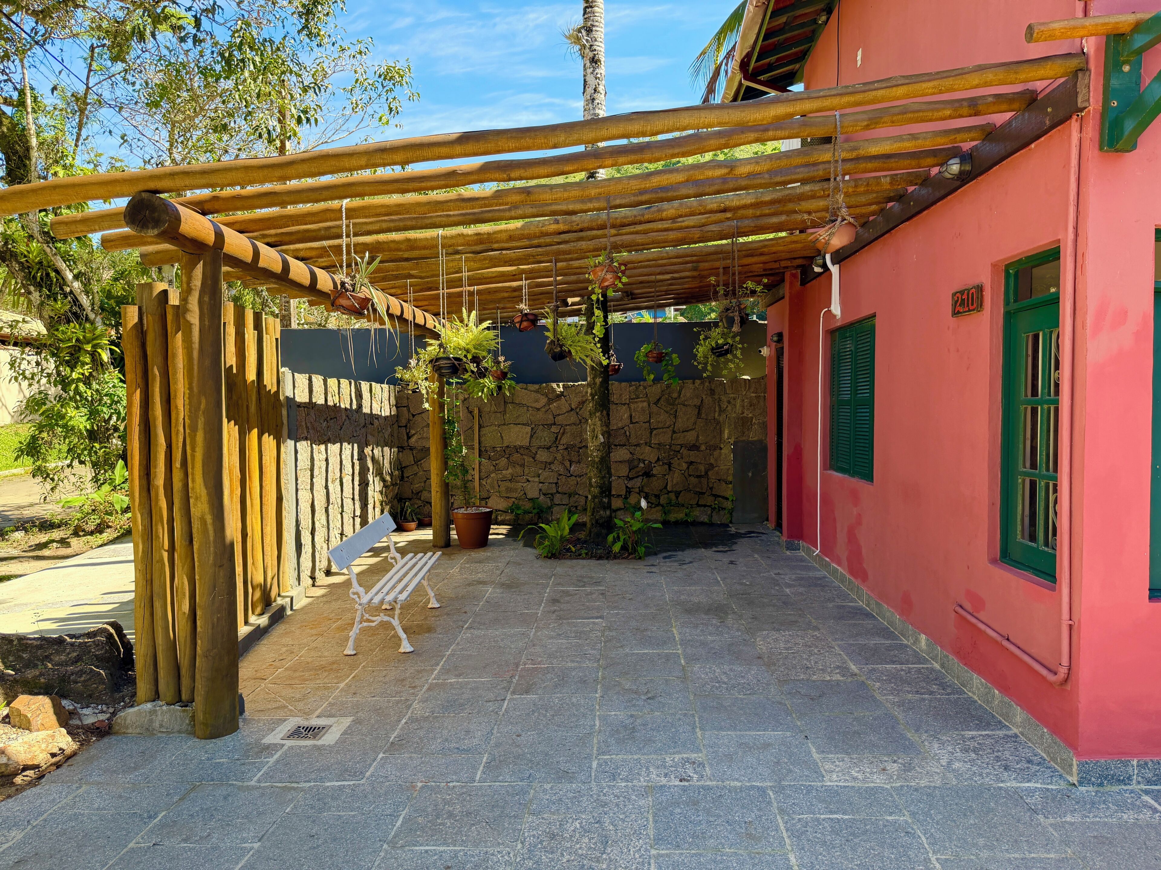 A covered patio with a stone wall, a bench, and hanging plants.