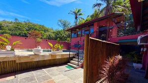 A pool area with a wooden deck, a staircase, and a red building in the background.