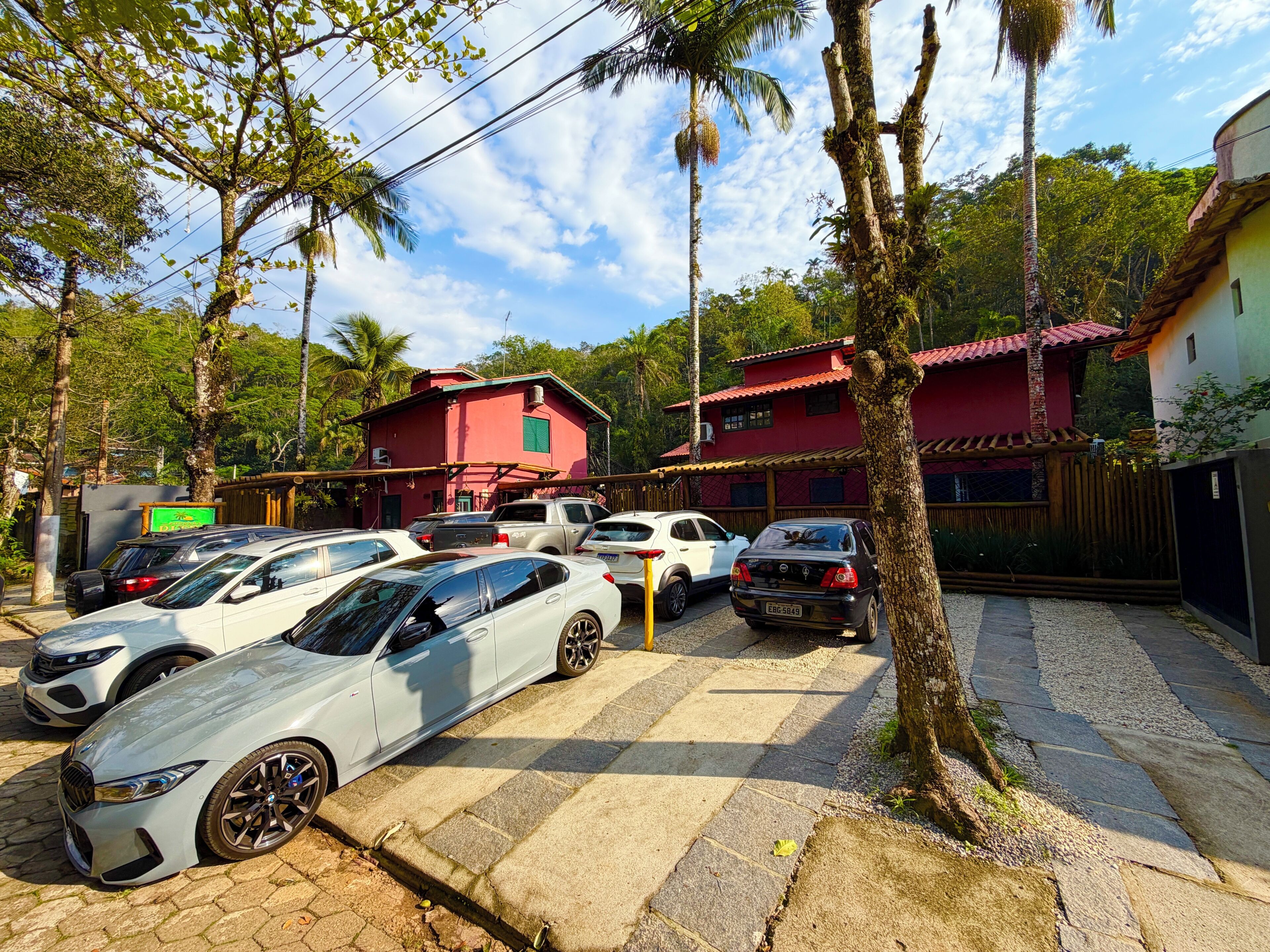 Un estacionamiento con varios autos, un edificio rojo y un árbol.