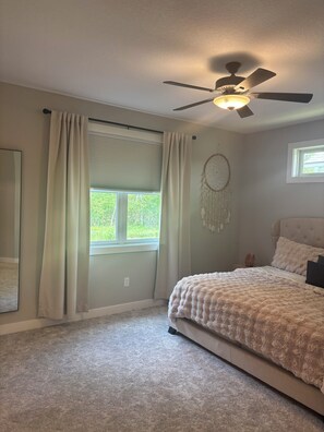 Un dormitorio con cama, ventilador de techo, atrapasueños y ventana con cortinas.