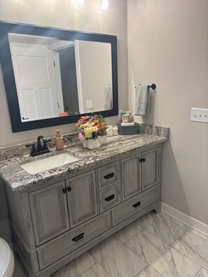 Un baño con lavamanos de encimera de granito, un espejo grande y un mueble con cajones.