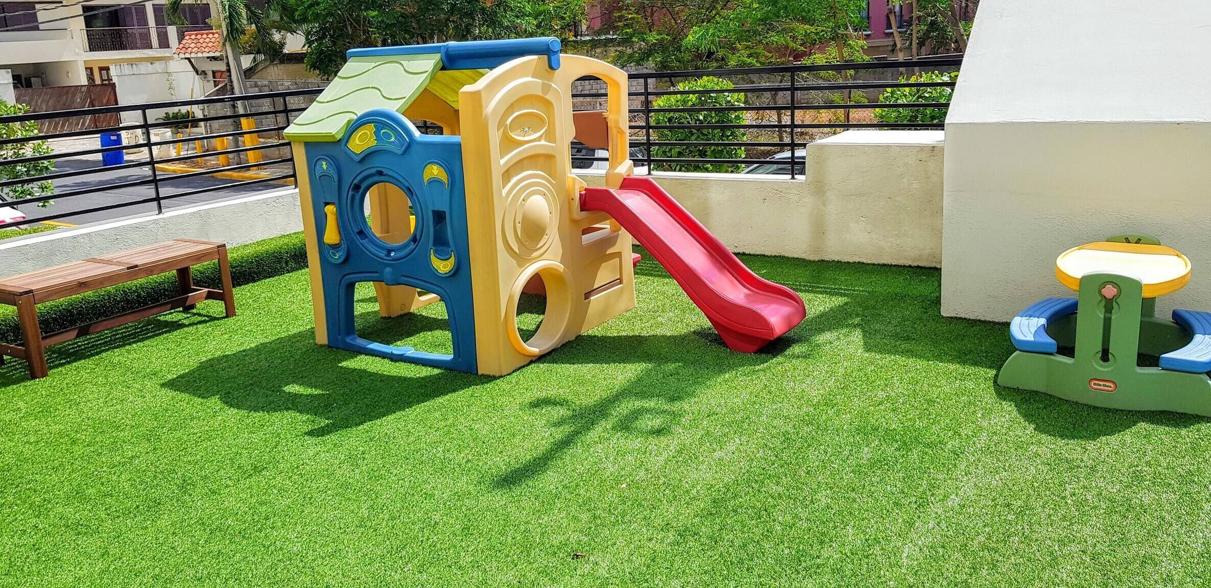 Une structure de jeux pour enfants avec un toboggan installé sur une surface d'herbe artificielle.