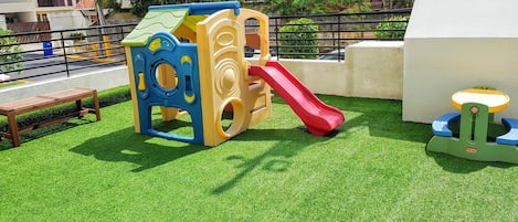 Une structure de jeux pour enfants avec un toboggan installé sur une surface d'herbe artificielle.