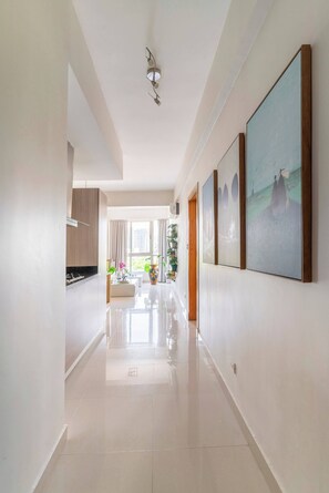 A hallway with a kitchen area on the left, a dining area with a table and chairs, and a living space with a sofa and a large painting on the right. - Stylish Downtown Kingbed 300mb Fast Wifi! (Santo Domingo)