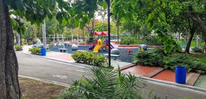 A playground with slides and play structures, surrounded by trees and a paved area. - Stylish Downtown Kingbed 300mb Fast Wifi! (Santo Domingo)