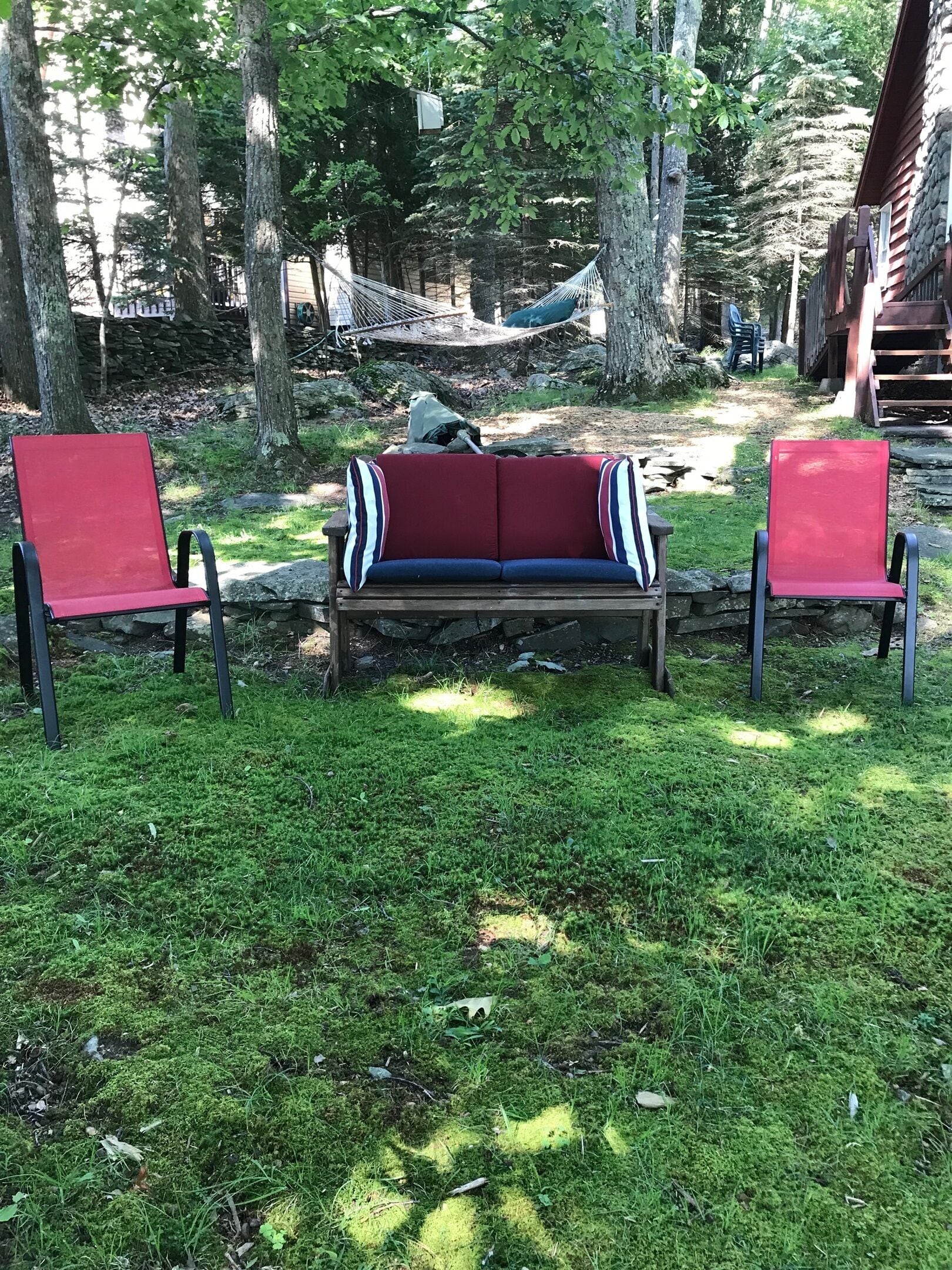 A wooden bench with a red cushion in a grassy area with trees.