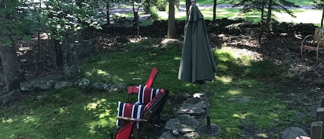 Un jardin avec un mur en pierre, une table de pique-nique couverte et deux chaises à rayures rouges et blanches.
