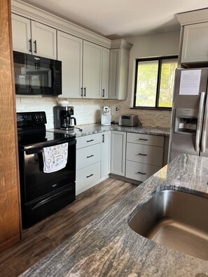 A kitchen with white cabinets, a black stove, a microwave, a coffee maker, a toaster, and a stainless steel sink.