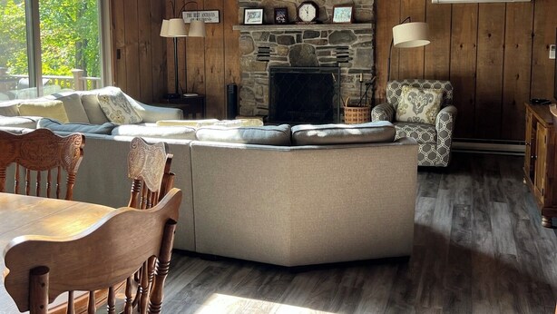 A cozy living room with a stone fireplace, wooden ceiling beams, and a large window. - Lakefront on Wallenpaupack with Hot Tub - Pet Friendly (Lakeville)