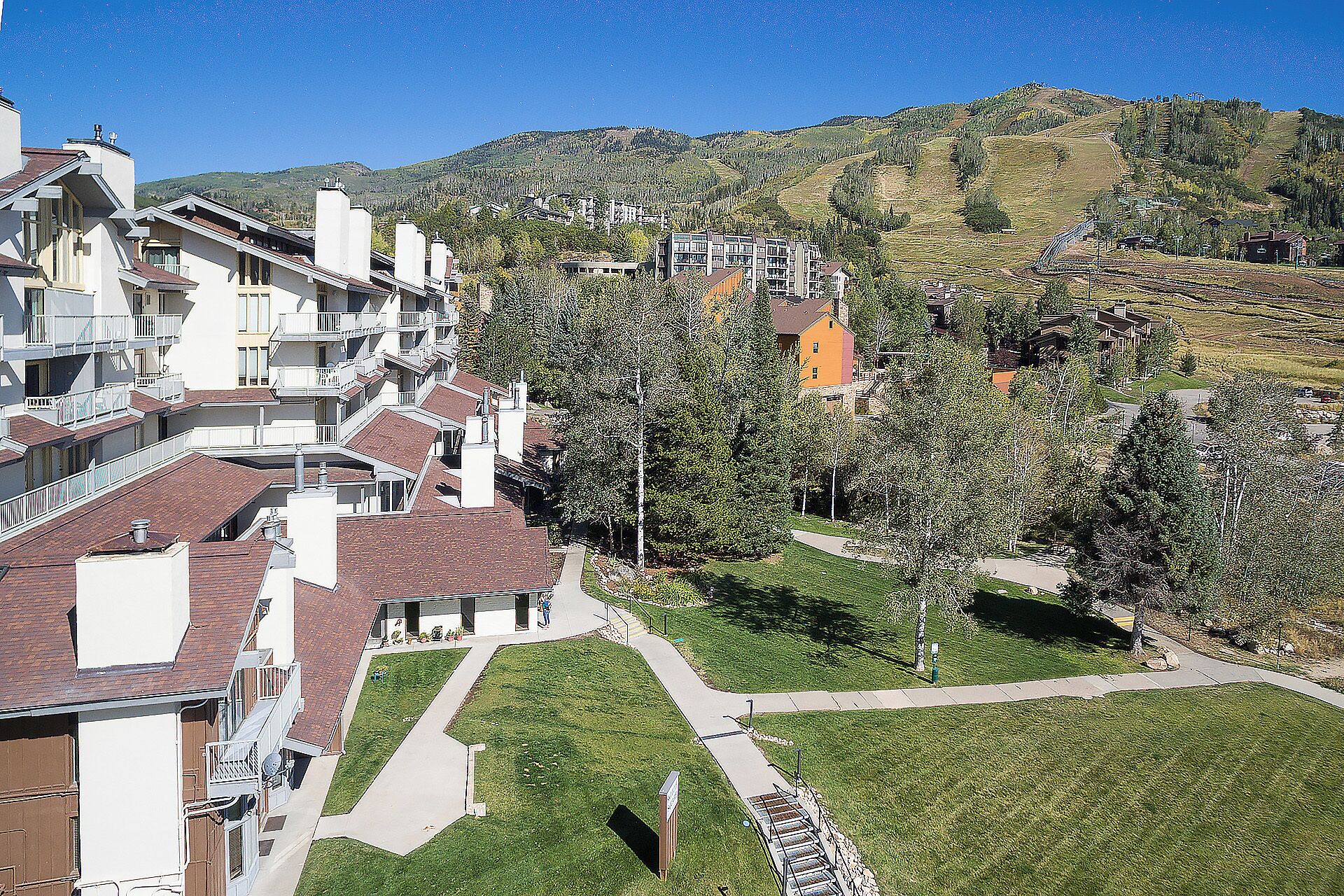 A residential area with modern houses, a well-maintained lawn, and a hilly backdrop.
