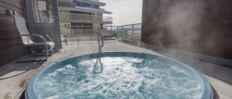 Un jacuzzi en una terraza de madera con vista a un edificio y un cielo nublado.