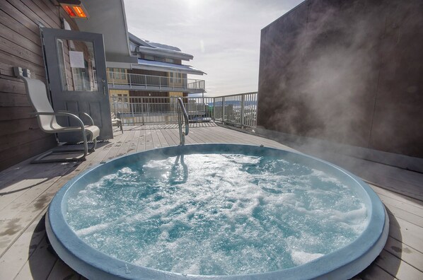 A hot tub on a wooden deck with a view of a building and a cloudy sky. - ST406 | Newly Modern| Close access + Across Street from Slopes (Steamboat Springs)