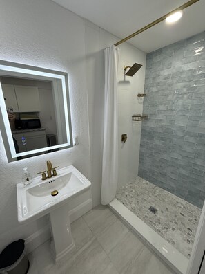 Un baño moderno con un lavamanos blanco, un espejo y una ducha con puerta de cristal.
