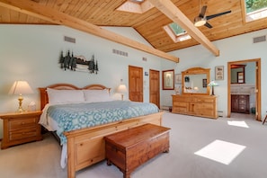 Une chambre à coucher avec un lit en bois, des tables de chevet, un banc, une commode, un miroir et un ventilateur de plafond.