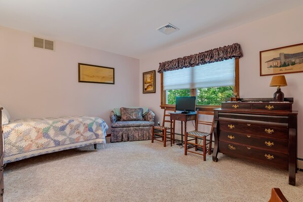 Une chambre à coucher avec un lit, un bureau avec un ordinateur, une commode et deux chaises.