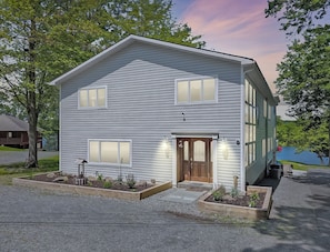 A two-story house with a front porch, a wooden door, and a small garden area with plants and a bird feeder. - Griffin Lakefront on Lake Wallenpaupack with Private Dock, AC - sleeps 10 (Greentown)