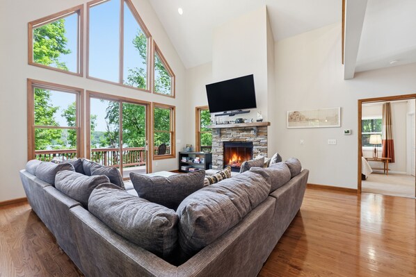 A spacious living room with a large gray sectional sofa, a stone fireplace, and a flat-screen TV mounted above it.