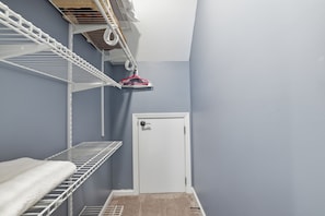 A narrow hallway with a white door, metal shelving units, and a hanging laundry rack.