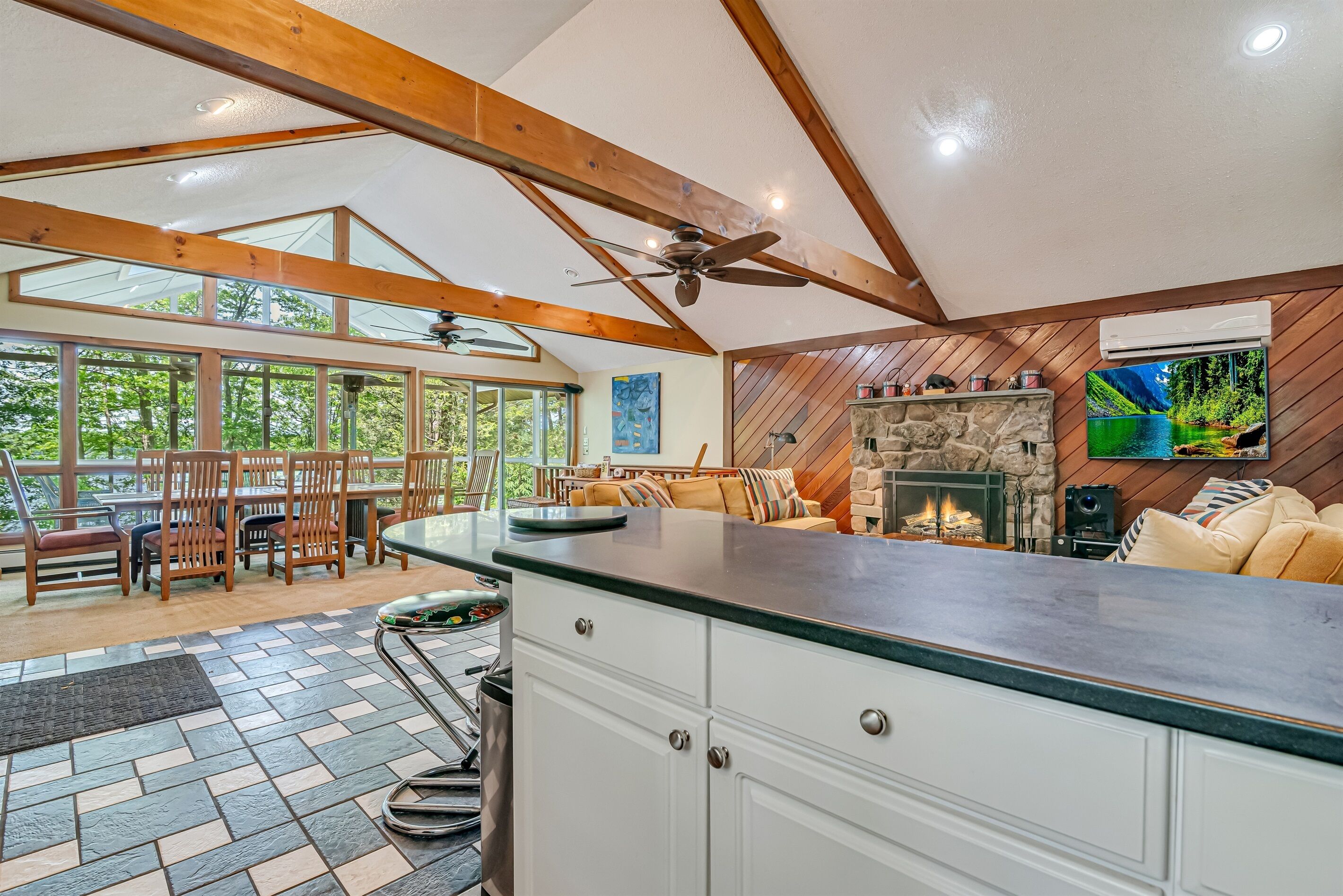 A spacious kitchen with a stone fireplace, wooden ceiling beams, and a large window overlooking a garden.