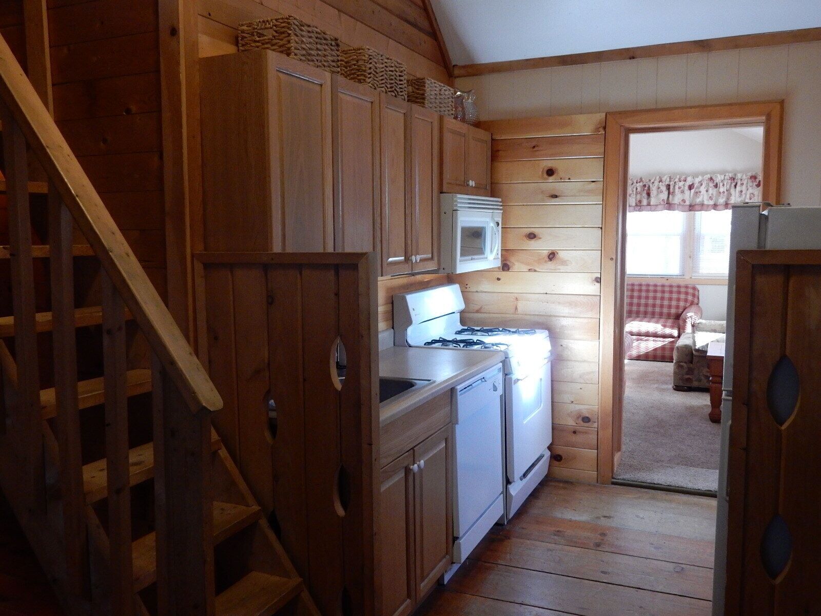 A wooden cabin interior with a kitchen area, including a stove, microwave, and cabinets.